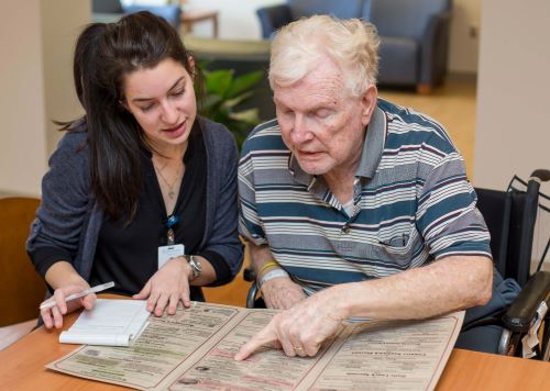 Female physical therapist helps male patient read a menu in speech therapy.